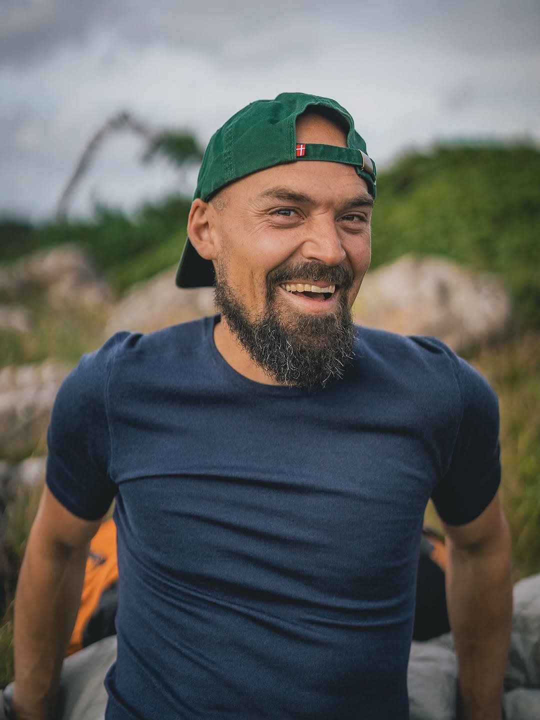 Rasmus Kragh griner i grøn kasket og mørkeblå t-shirt med klipper og grønt bag sig