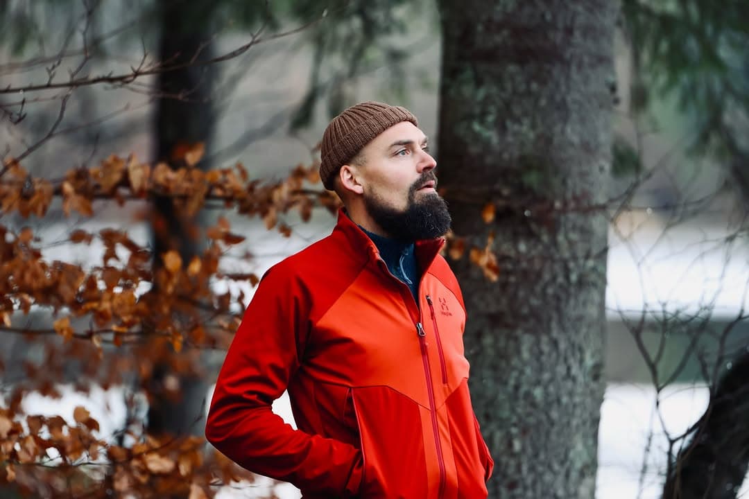 Rasmus Kragh i rød jakke står eftertænksomt mellem træerne i en efterårsskov